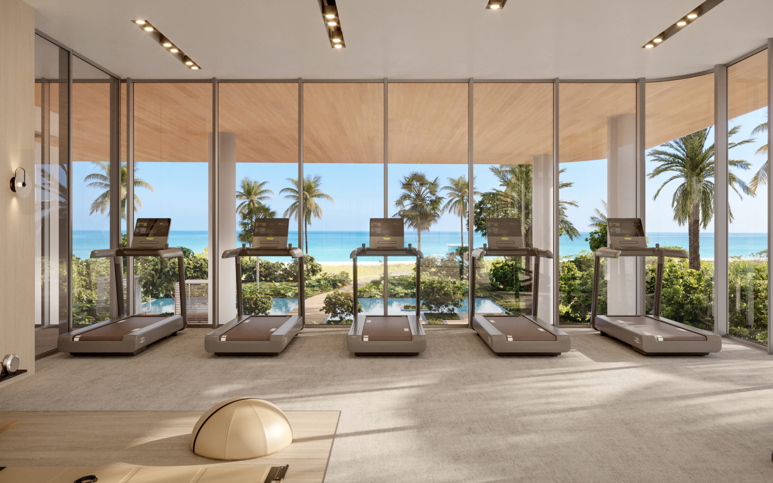 Treadmills in fitness center with view of the ocean and palm trees at Ocean Front Surfside luxury condos in Miami.